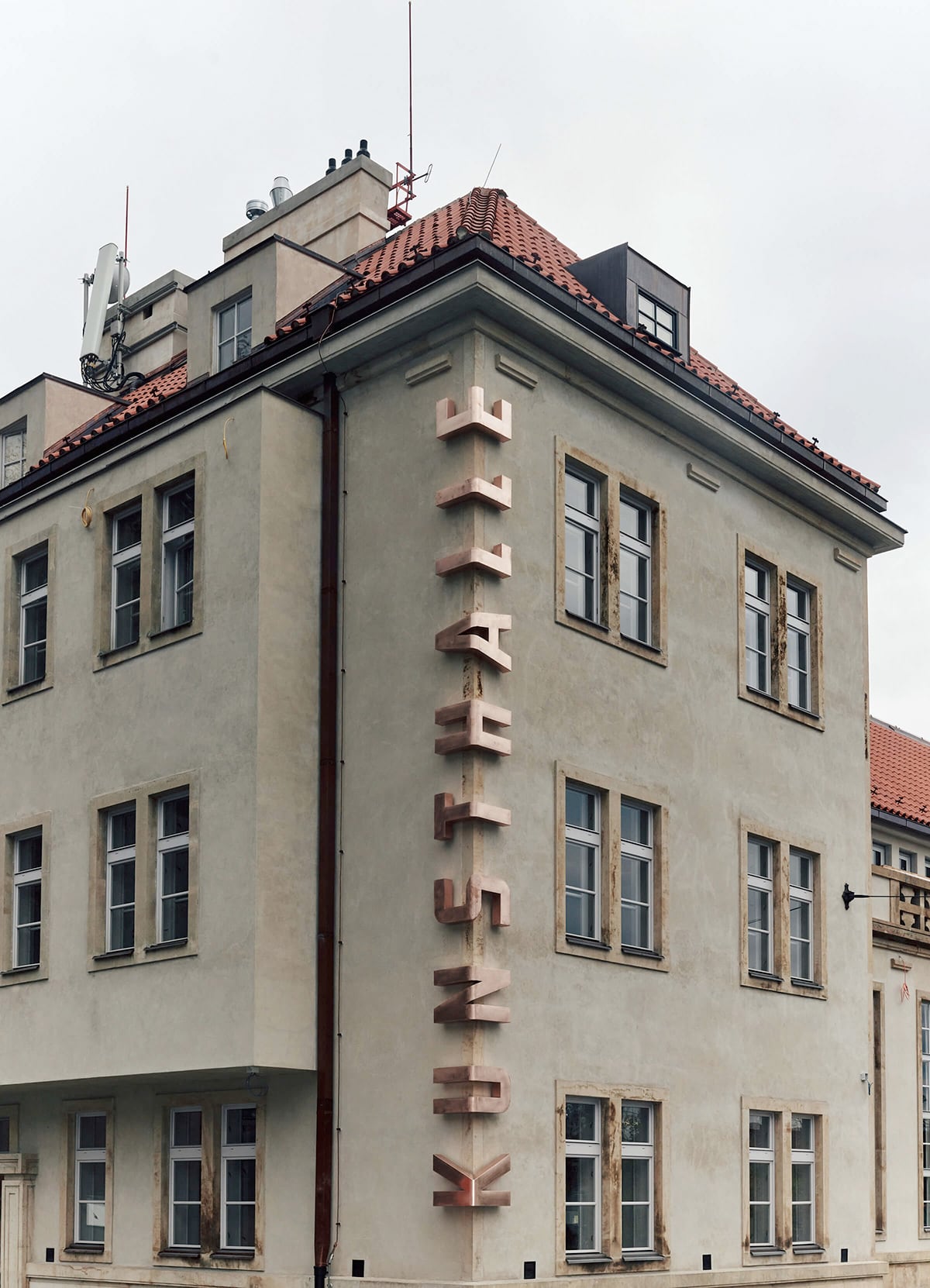A Chunky Bronze Logo Wraps Around the Corner of a Prague Art Museum